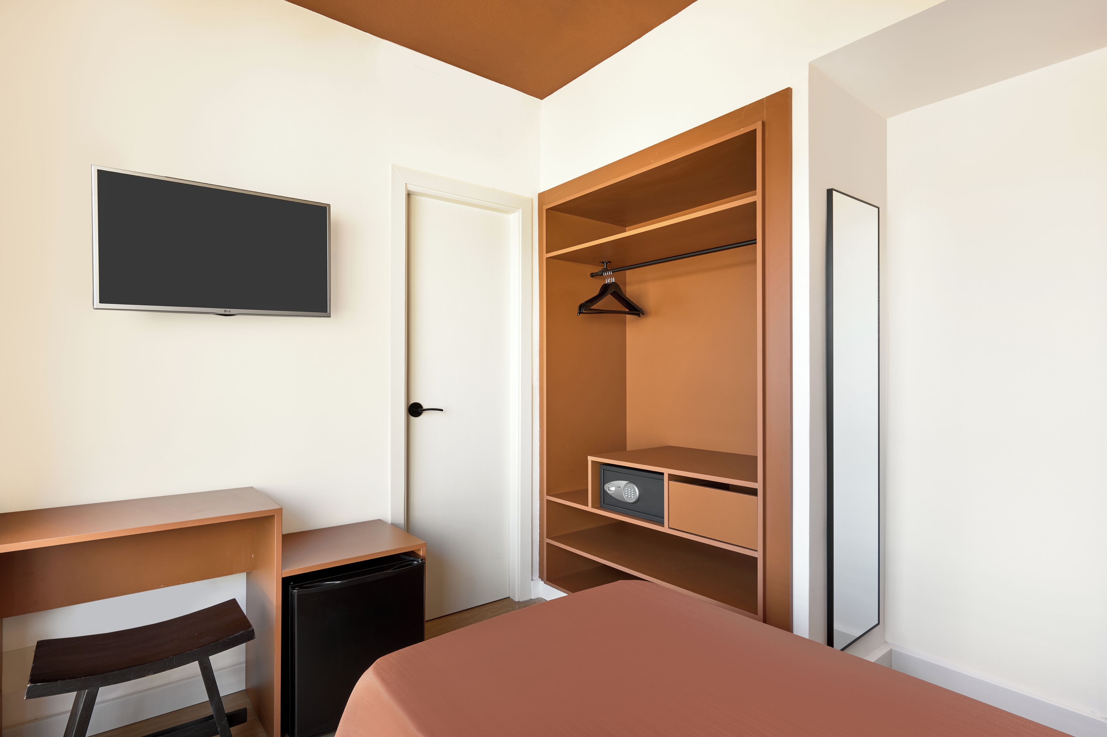 A bedroom with a bed, a desk, a chair, a TV, a wardrobe, and a small cabinet.