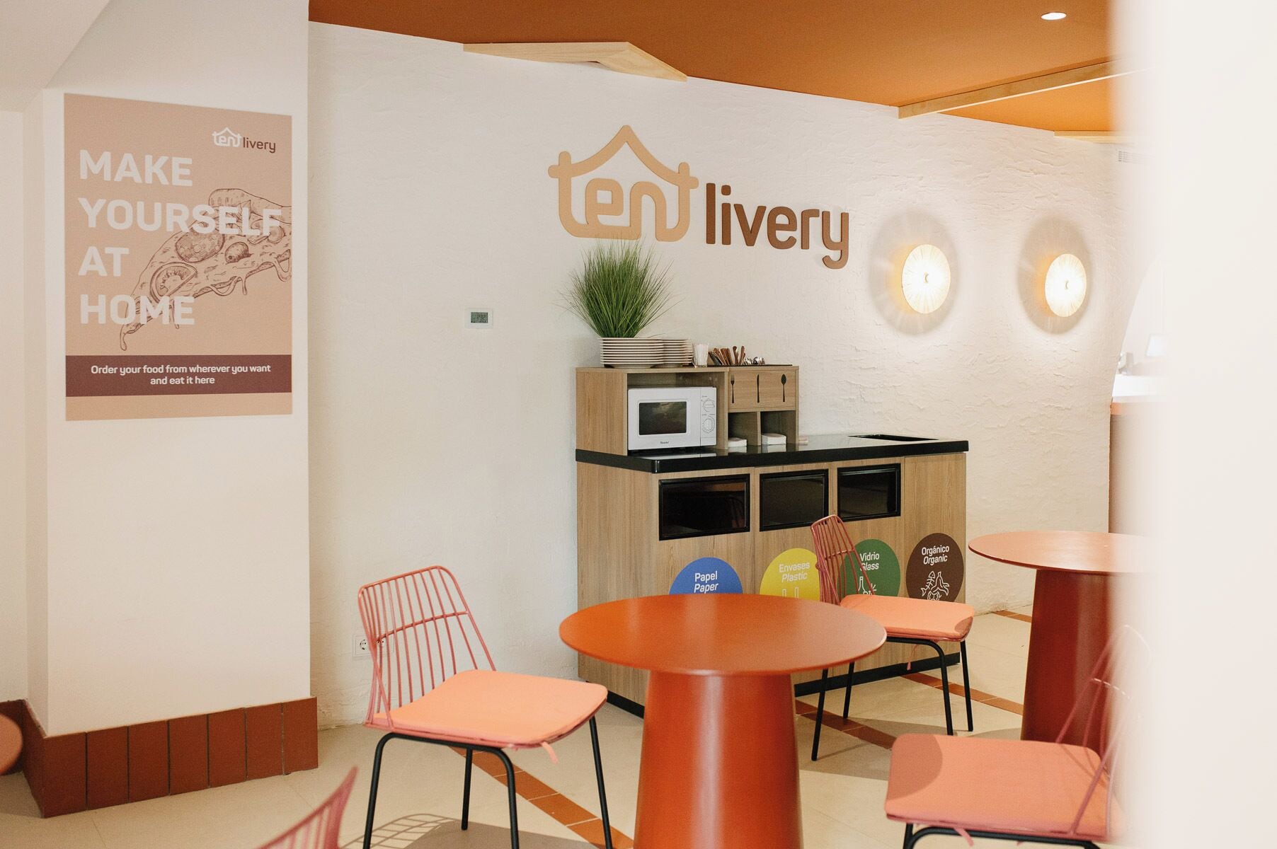 A cozy interior with a 'ten livery' sign, wooden cabinets, a microwave, and orange chairs.