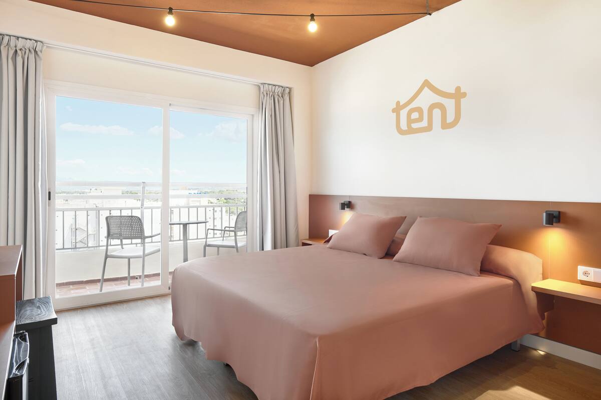 Une chambre d’hôtel avec un grand lit, un balcon avec des chaises et une vue sur la ville.