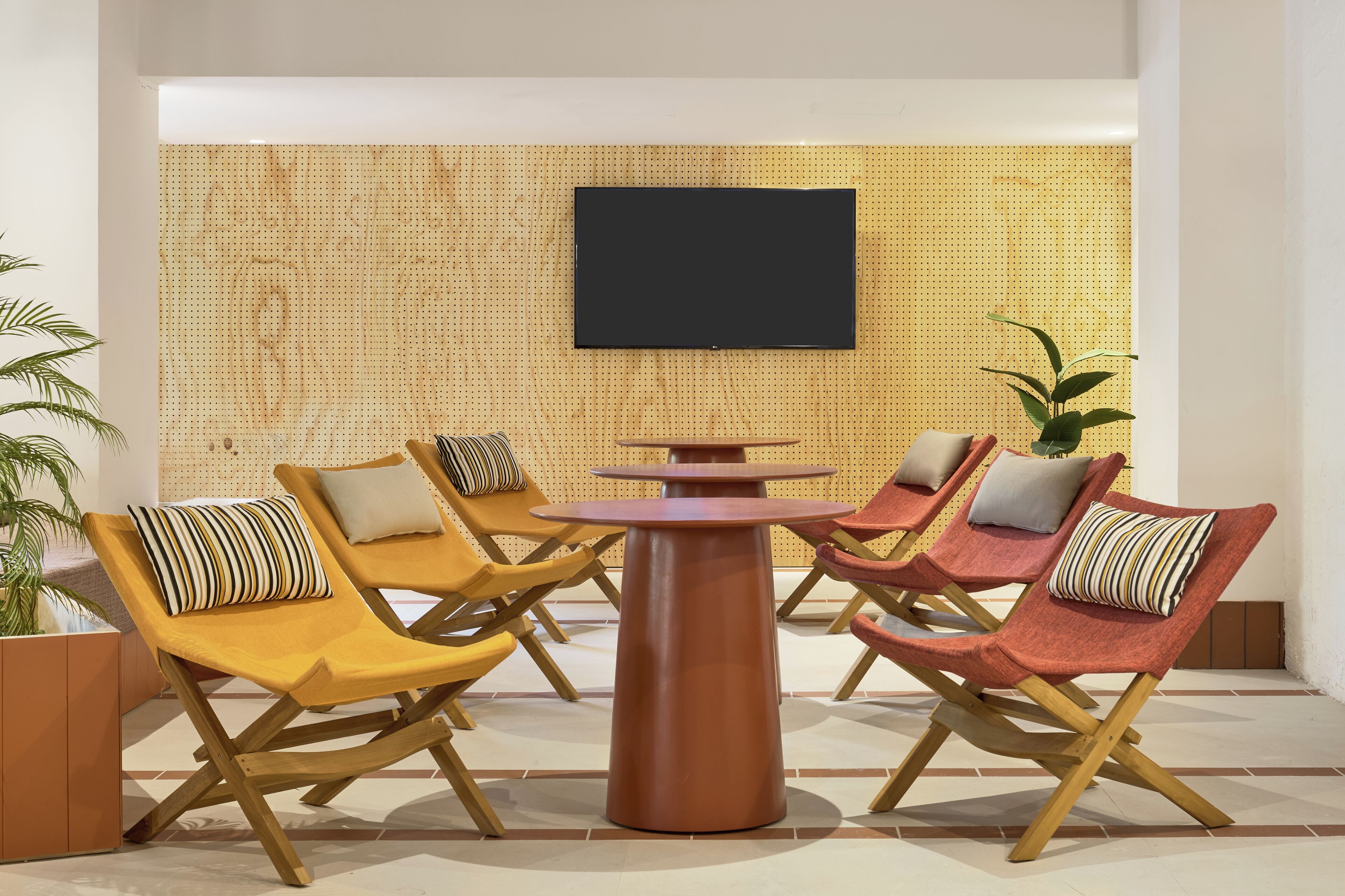 A seating area with four lounge chairs, a central table, and a mounted television on a wooden wall.