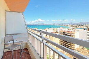 Un balcón con mesa y silla, con vistas a una ciudad costera que incluye edificios y montañas a lo lejos.