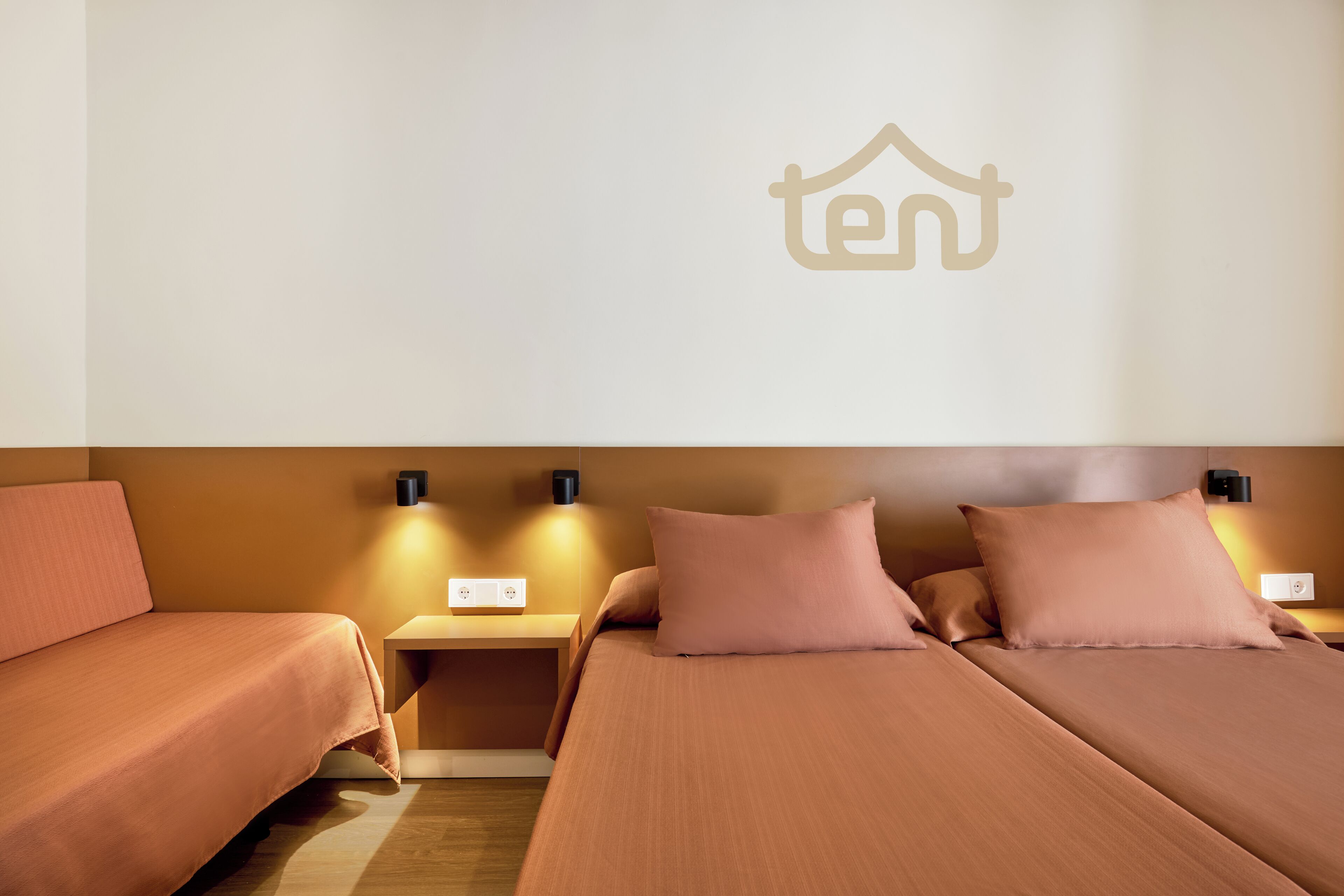 A hotel room with two beds, a wall-mounted logo, bedside lamps, and a nightstand.