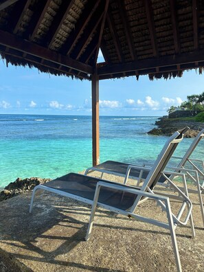 A beachside lounge with a thatched roof, overlooking a clear blue sea and rocky shoreline. - Nasama Resort (Port Vila)