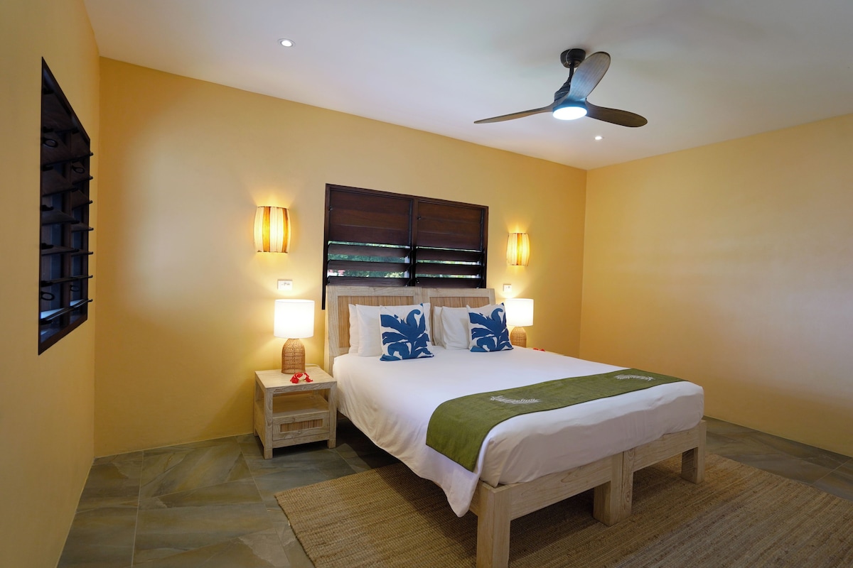 A bedroom with a bed, nightstands, a ceiling fan, and wall-mounted lamps.