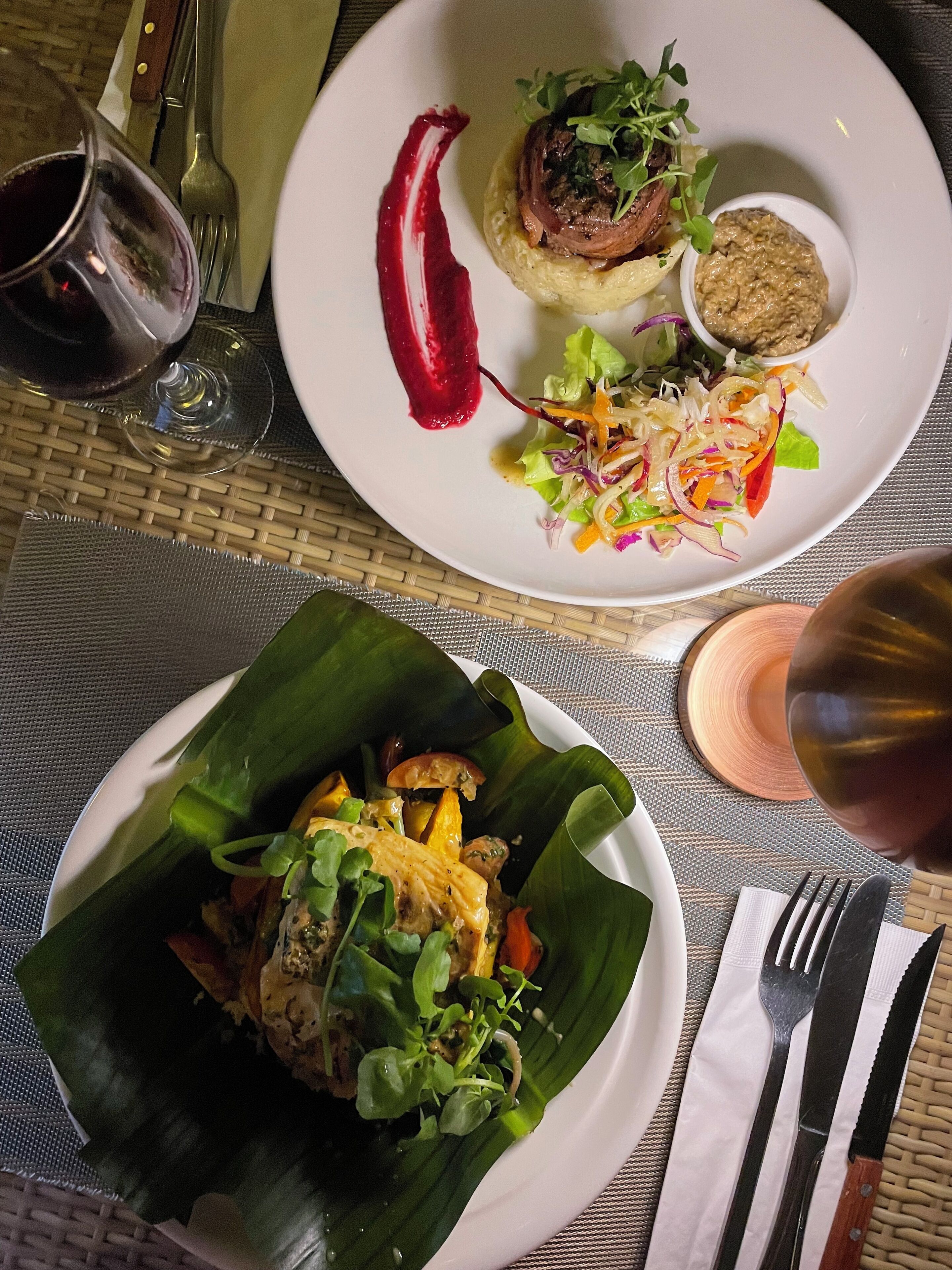A table set with two plates of food, a glass of red wine, and cutlery.