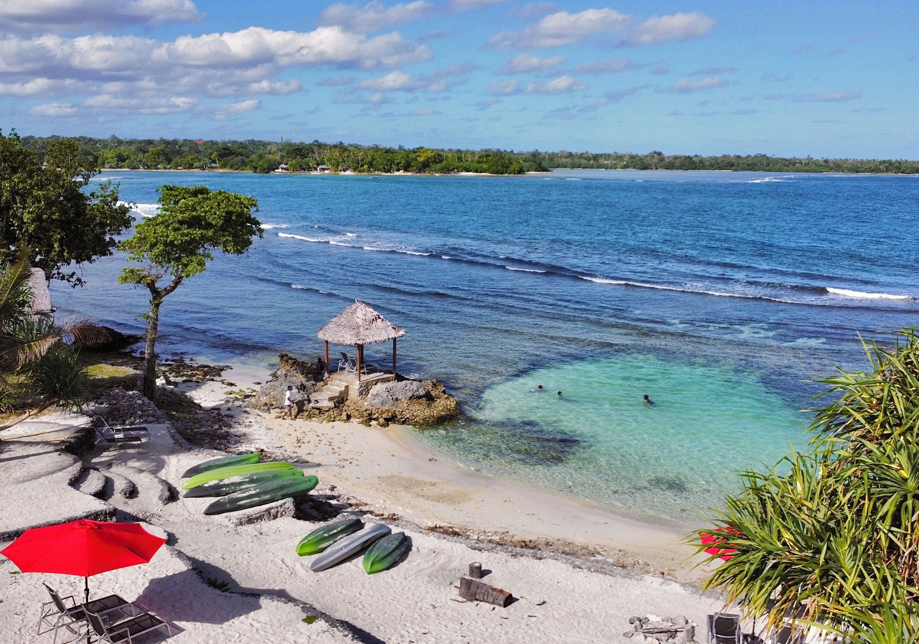 A beach with clear turquoise water, a thatched-roof hut, and several green canoes.
