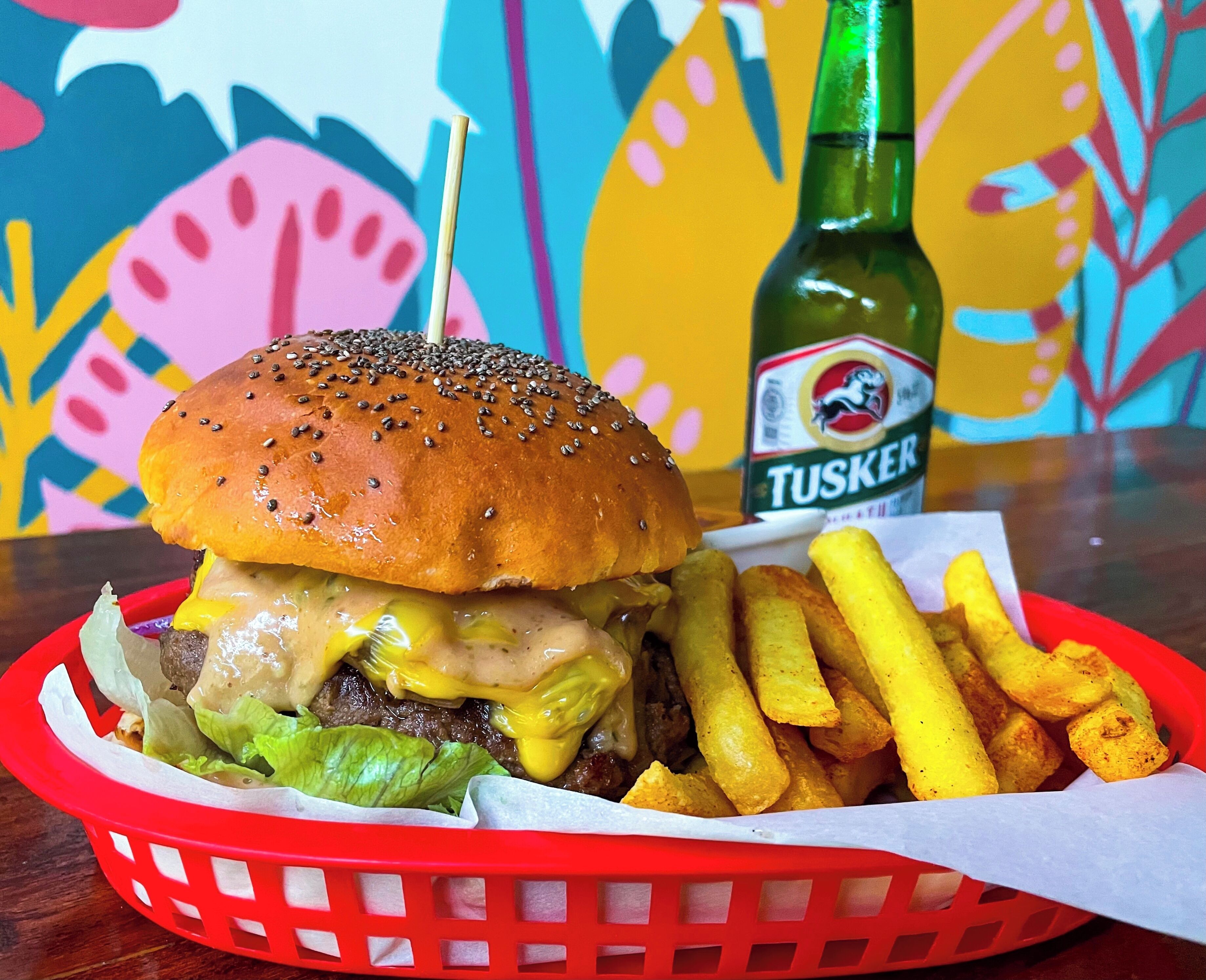 Una hamburguesa con papas fritas y una botella de cerveza Tusker sobre una mesa.