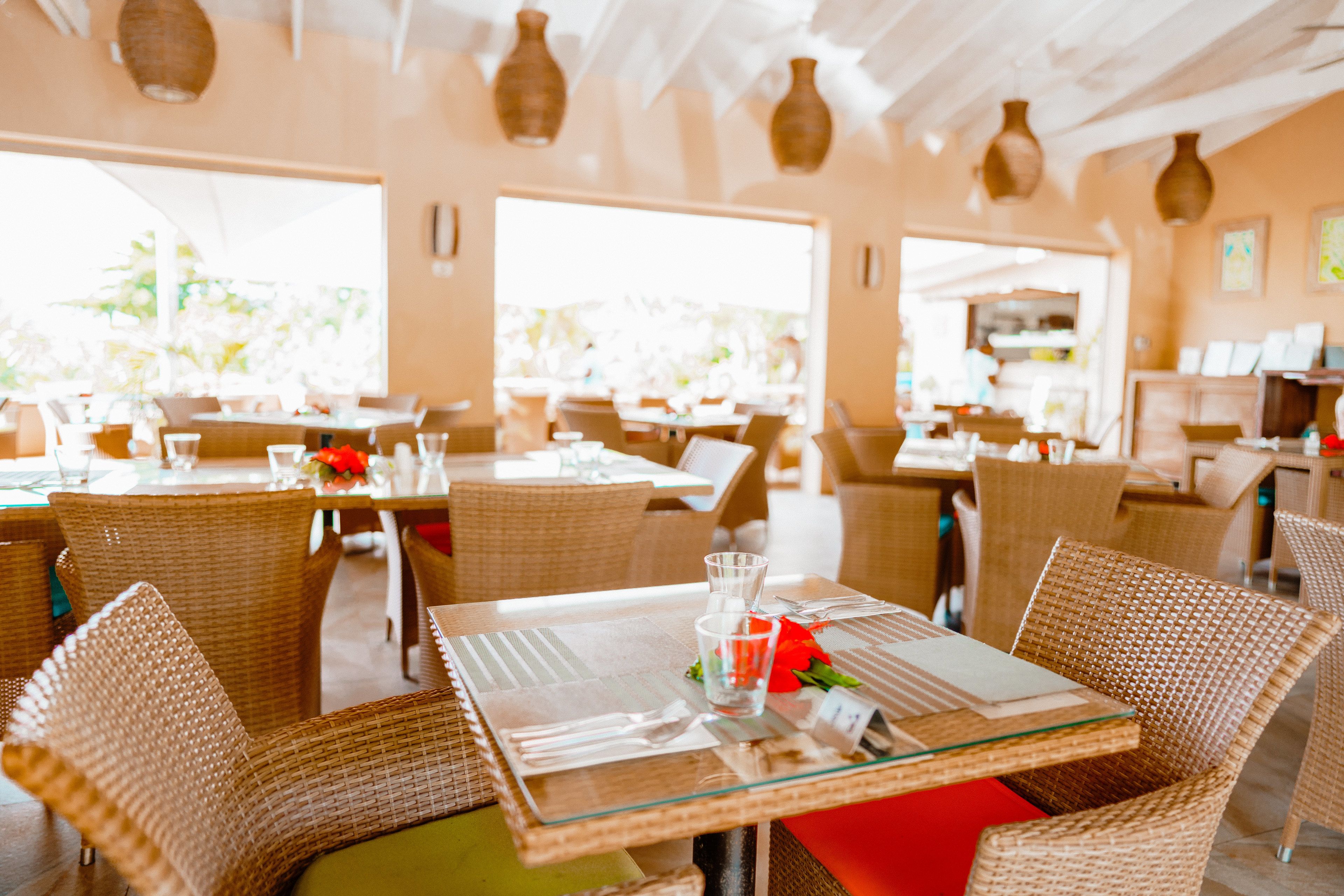 Un restaurante con mobiliario de mimbre, mesas de vidrio y amplios ventanales.