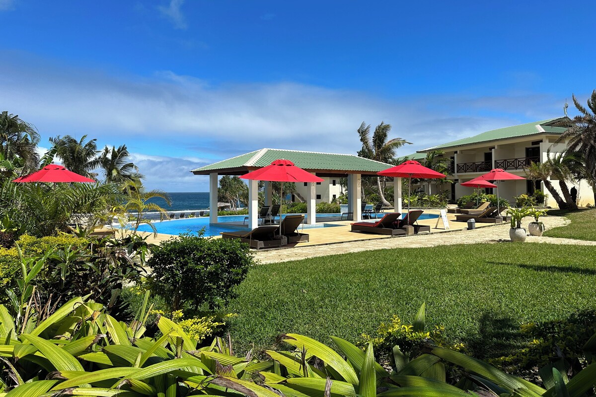A resort with a pool, red umbrellas, and a view of the ocean.