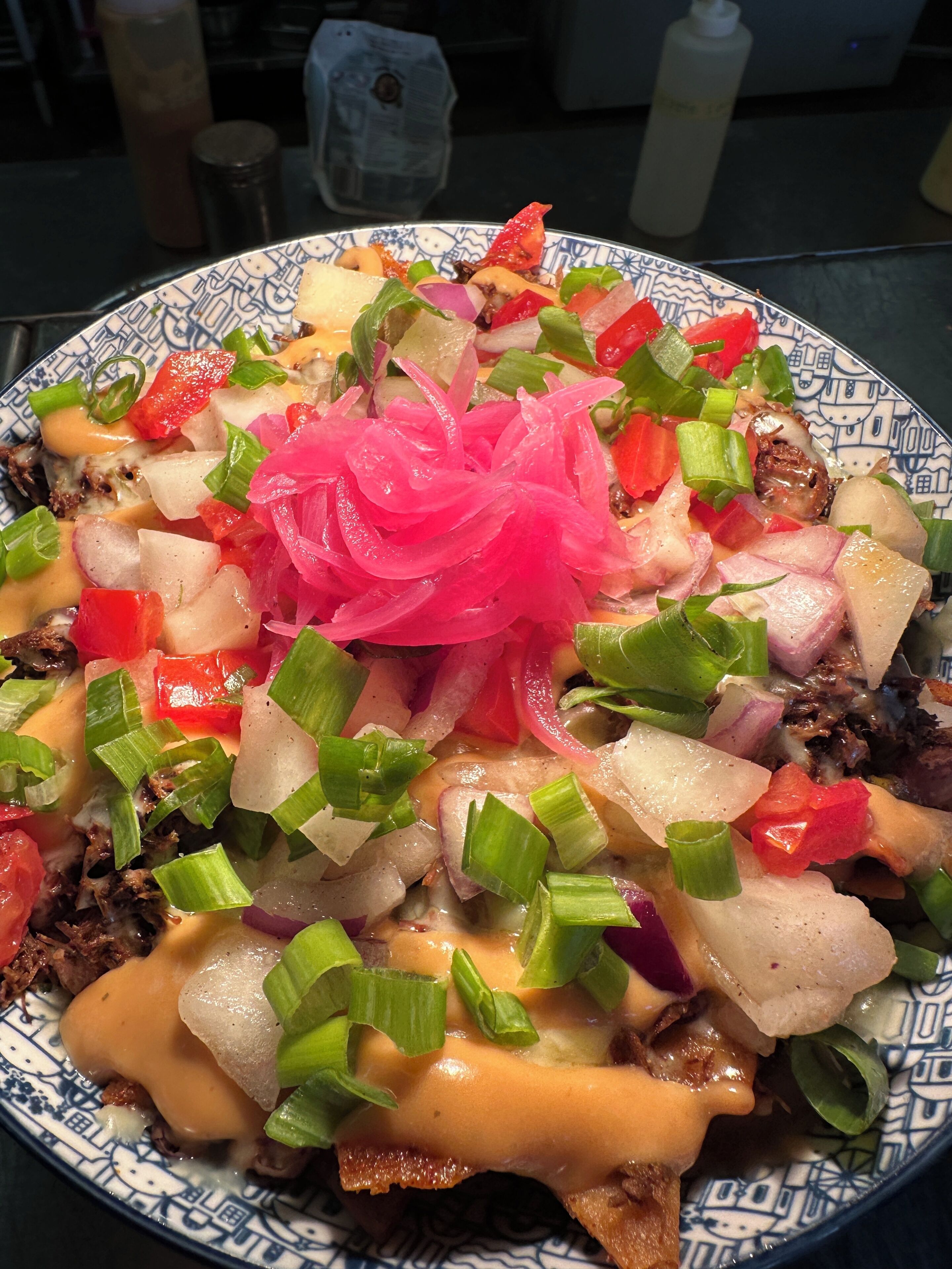 Un plato de nachos cubierto de queso, cebollas, pimientos y una guarnición de cebolla rosa.