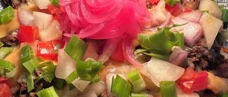 Un plato de nachos cubierto de queso, cebollas, pimientos y una guarnición de cebolla rosa.