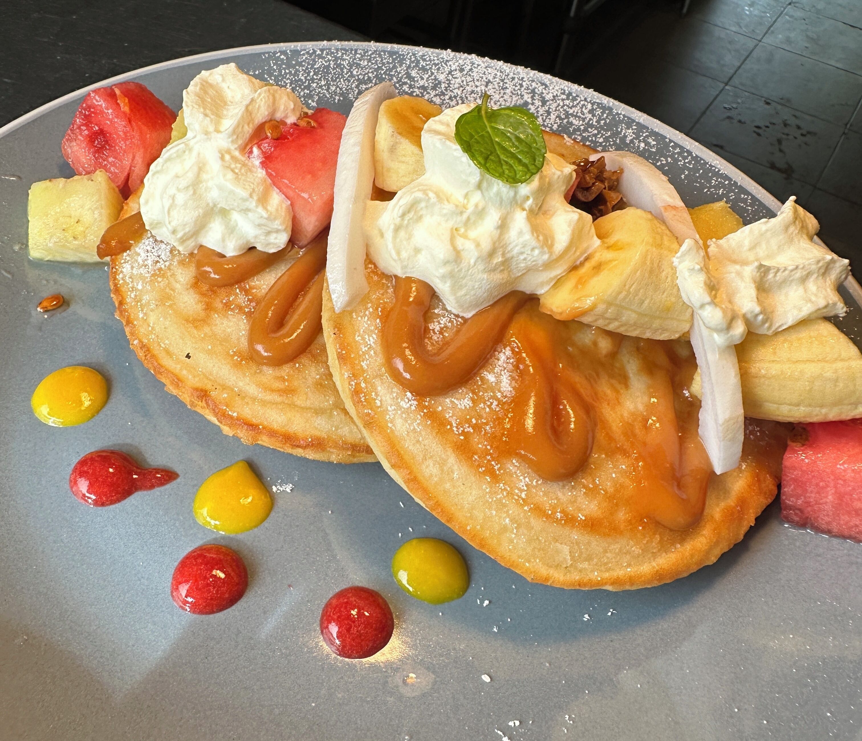 A plate with pancakes topped with whipped cream, caramel, and fruit.
