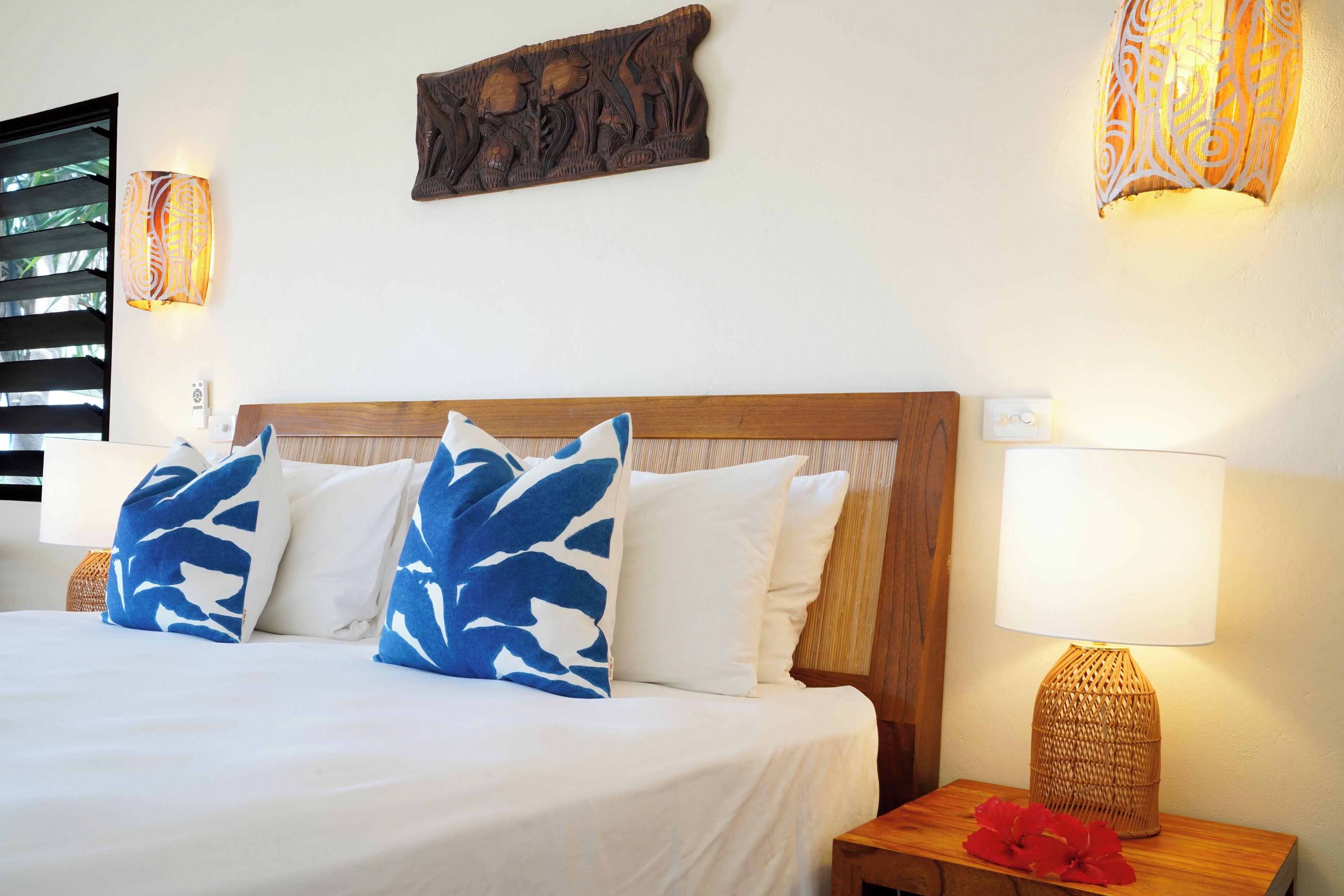 A neatly made bed with white and blue patterned pillows, a wooden headboard, and a bedside lamp with a woven base.