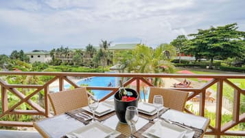A dining table set with white plates, cutlery, and wine glasses, overlooking a pool and a tropical landscape.