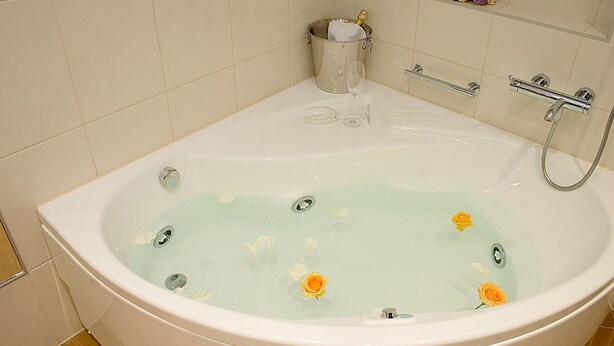 A large bathtub with a champagne bottle, glasses, and flowers in the water.