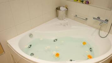 A large bathtub with a champagne bottle, glasses, and flowers in the water.