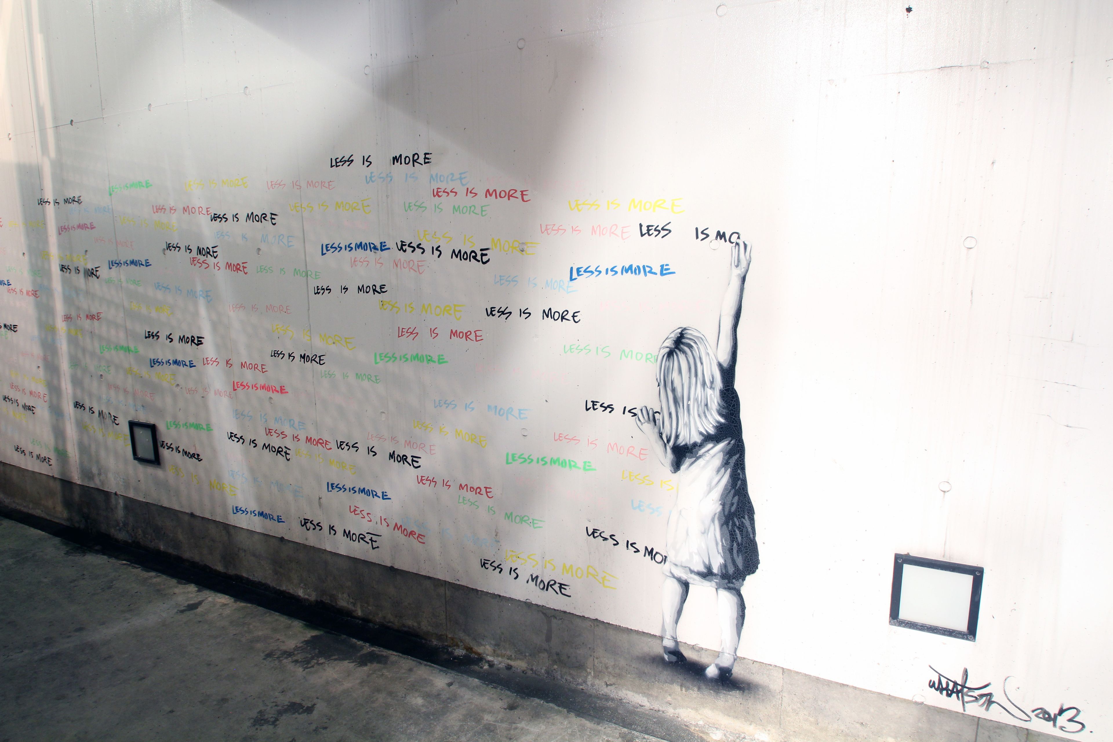 A wall with repeated text 'LESS IS MORE' and a mural of a person reaching up.