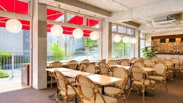 A restaurant with wicker chairs and tables, large windows, and a ceiling fan.
