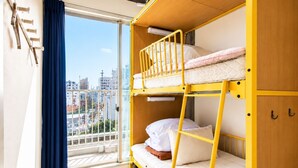 Habitación con literas, vista a la ciudad, una ventana con cortinas y un armario de madera con ganchos.