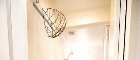 A narrow hallway leading to a shower area with a ceiling-mounted showerhead and a door on the right.