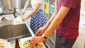 Una cocina con electrodomésticos de acero inoxidable, una tabla de cortar con verduras picadas y una botella de cerveza.