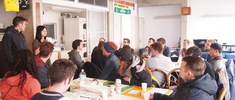 A group of people in a meeting room with tables, chairs, and a whiteboard.
