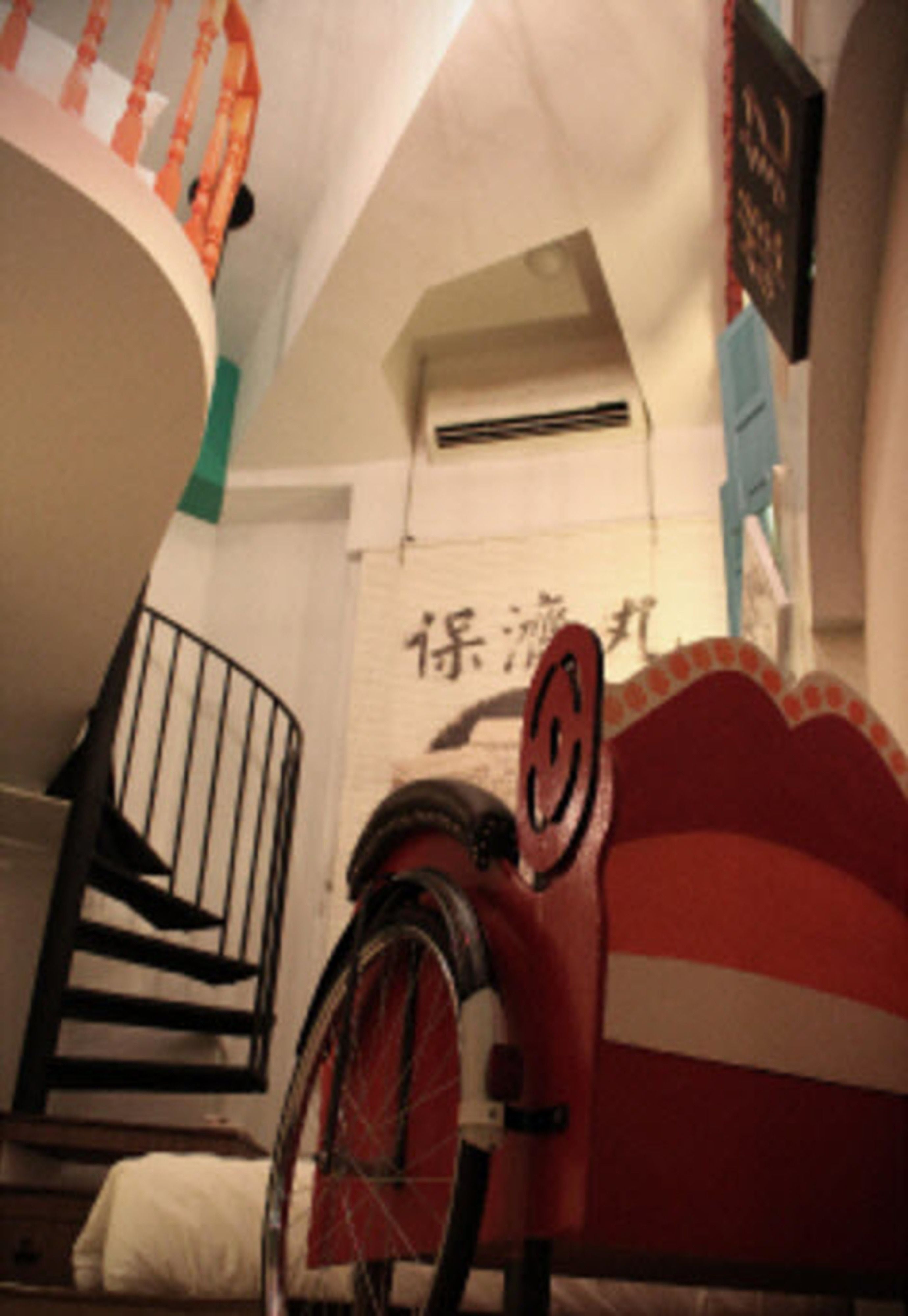 Un escalier avec un mur à rayures rouges et blanches, une rampe noire et un vélo appuyé contre le mur.