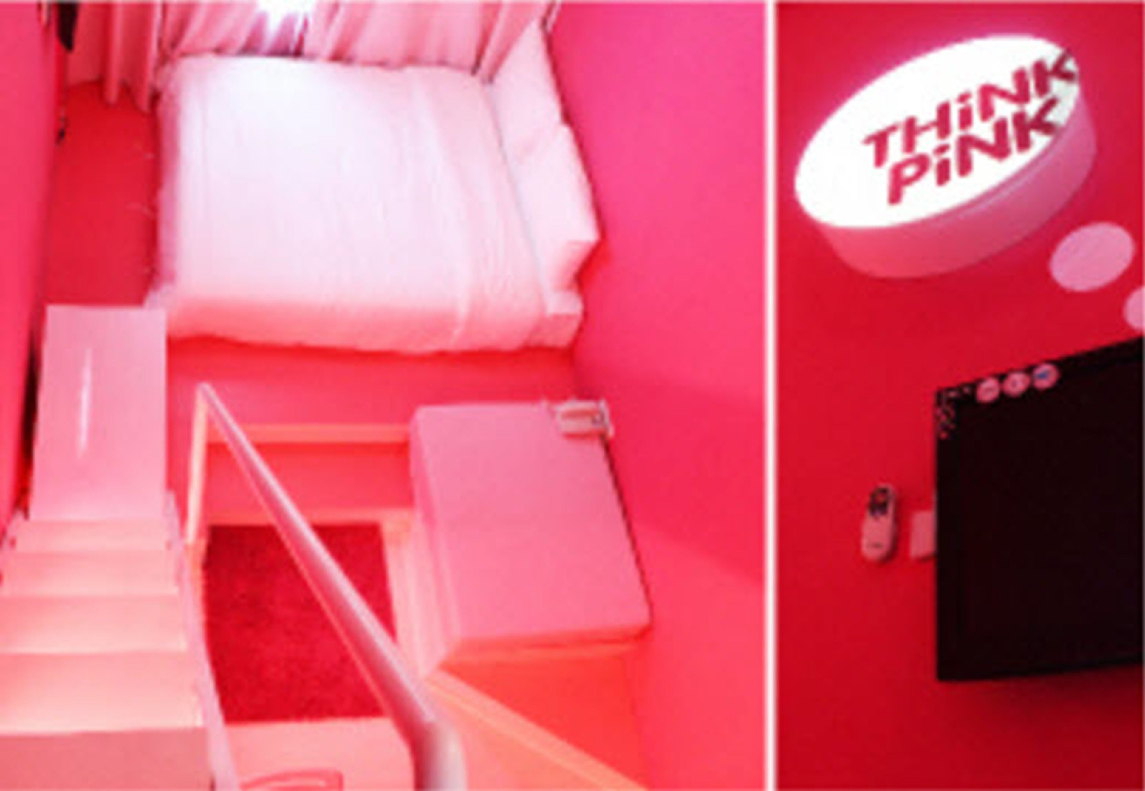 Een kamer in roze tinten met een bed, een klein tafeltje en een tv aan de muur.