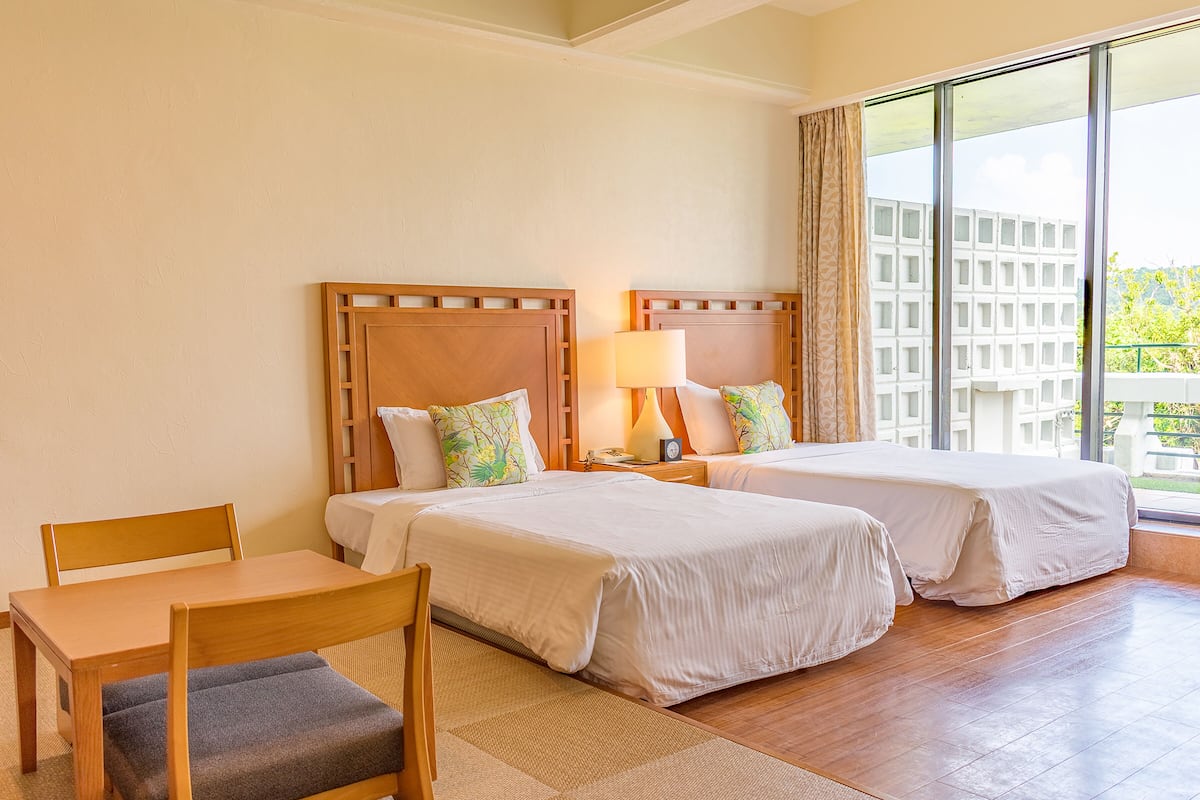A hotel room with two beds, a table, and a chair.