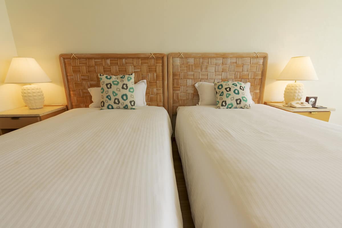 Two single beds with a woven headboard, each with a bedside table, a lamp, and a telephone.