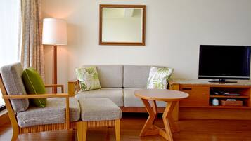 A living room with a sofa, armchair, and a small round table. A TV is on a wooden stand to the right.