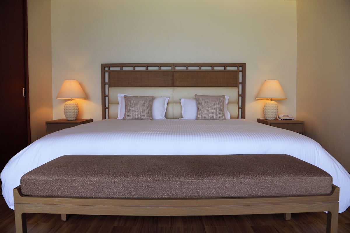 A large bed with a wooden headboard, two bedside tables with lamps, and a bench at the foot of the bed.