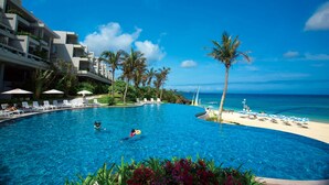 A swimming pool with lounge chairs and palm trees, adjacent to a beach and ocean view. - THE MOON BEACH MUSEUM RESORT (Onna)