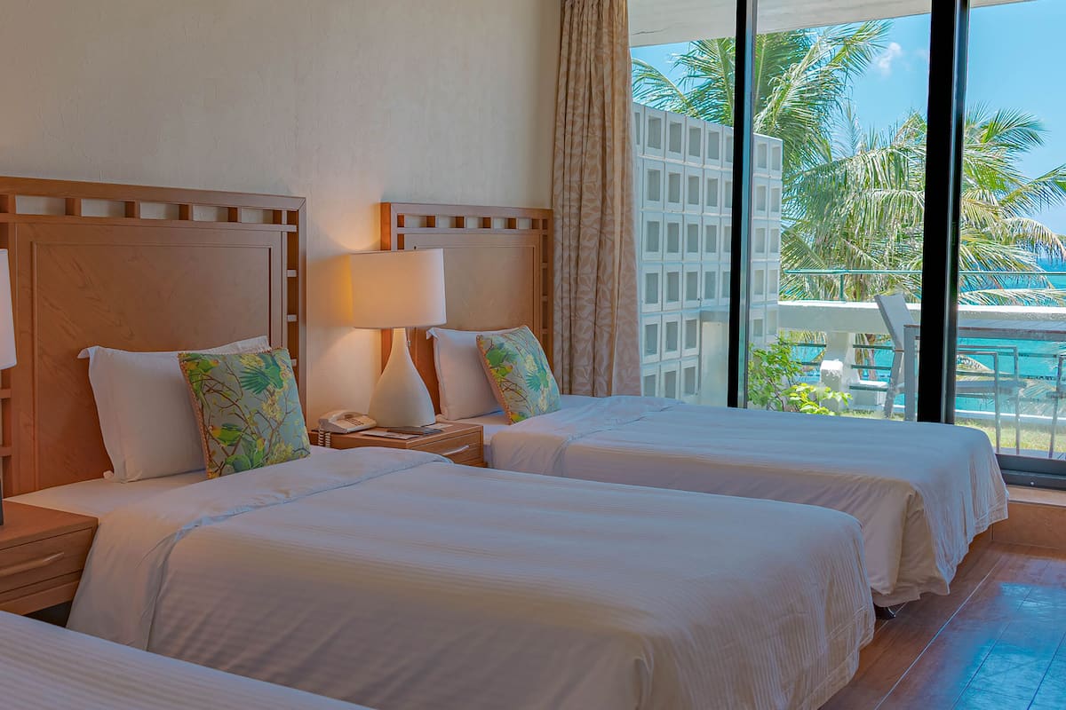 A hotel room with two beds, each with a wooden headboard, white linens, and a bedside table with a lamp and a phone.