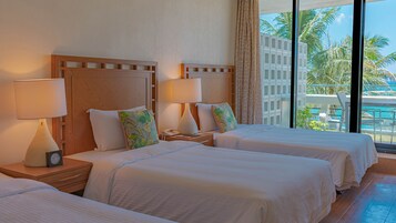 Habitación de hotel con dos camas, cada una con cabecero de madera, ropa de cama blanca y una mesita de noche con lámpara y teléfono.