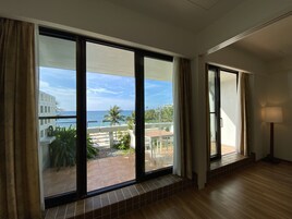 A room with large sliding glass doors leading to a balcony with a view of the sea and palm trees.