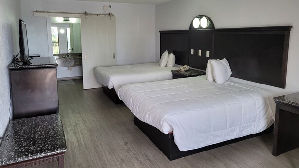 Une chambre d’hôtel avec deux lits, un bureau, un miroir et une salle de bain visible à travers une porte ouverte.