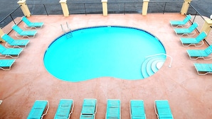 Une piscine à bordures incurvées, entourée d’une clôture en métal noir et agrémentée de plusieurs chaises longues bleues.