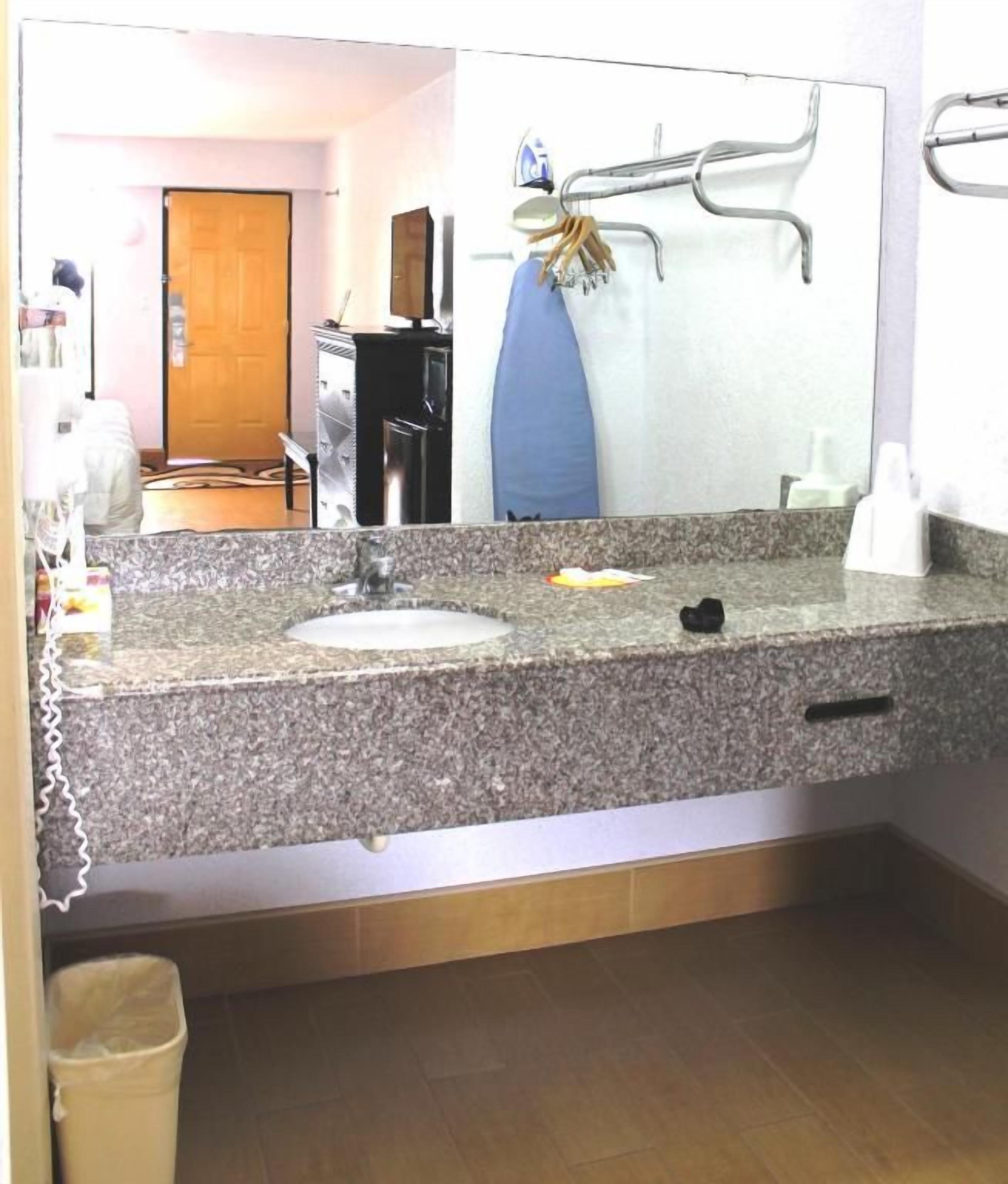Un baño con encimera de granito, un lavabo, un espejo y un perchero para toallas.
