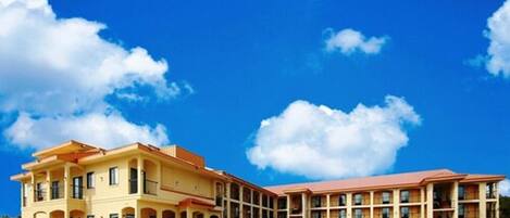 A hotel with a two-story structure, multiple balconies, and a parking lot with cars.