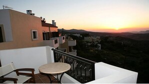A balcony with a table and chairs, overlooking a sunset with distant mountains. - Marina Hotel (Anogia)