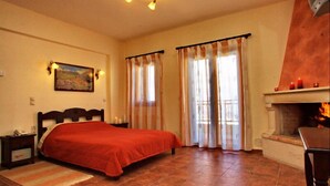 A bedroom with a bed, curtains, a fireplace, and a painting on the wall. - Marina Hotel (Anogia)