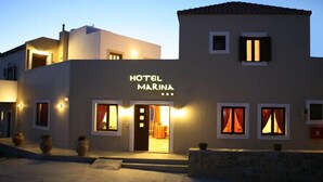 A hotel named "HOTEL MARINA" with a modern facade, multiple windows with curtains, and a well-lit entrance. - Marina Hotel (Anogia)