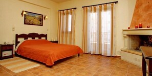 A bedroom with a bed, curtains, a fireplace, and a painting on the wall. - Marina Hotel (Anogia)