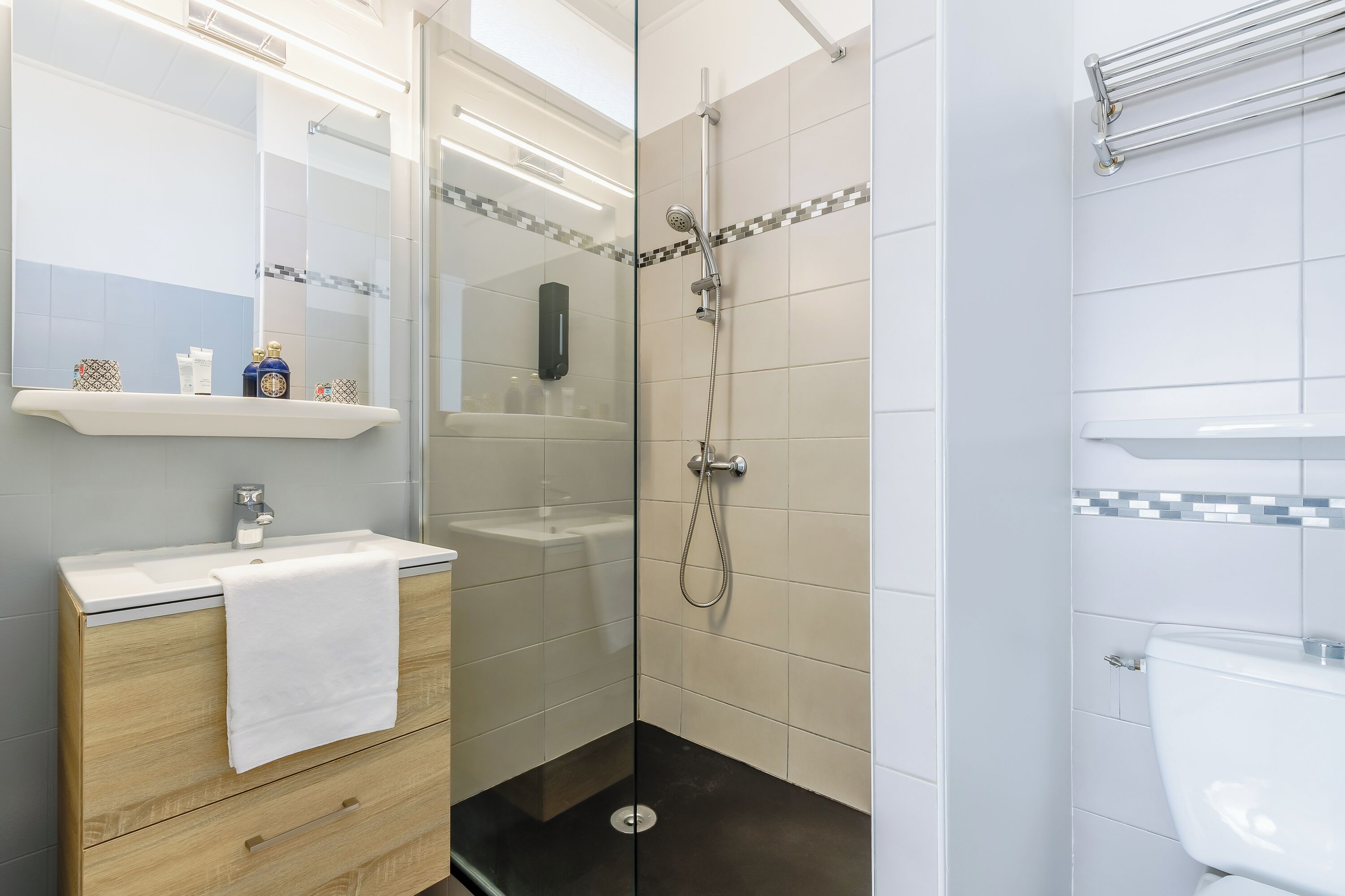 Un baño moderno con ducha de vidrio, un lavamanos blanco con una toalla y un inodoro.