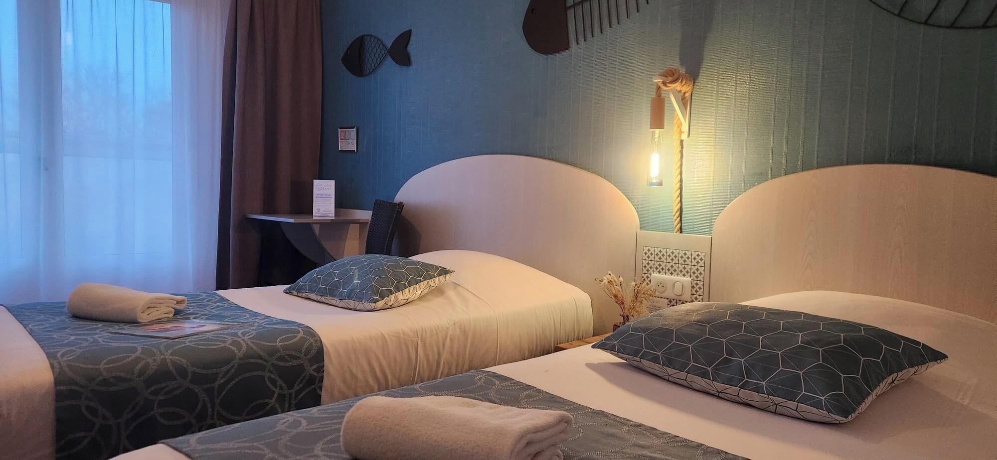 Une chambre d’hôtel avec deux lits, un bureau et une lampe fixée au mur.