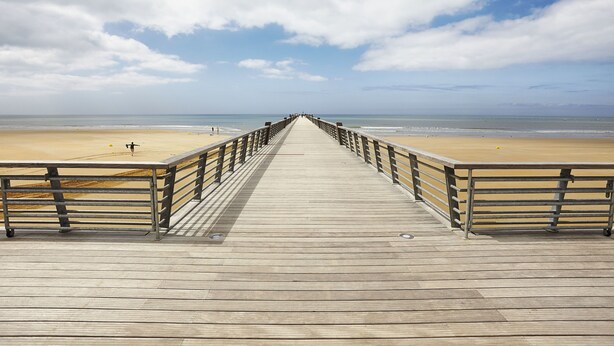 Une promenade en bois menant à une plage, avec une rambarde métallique de chaque côté.