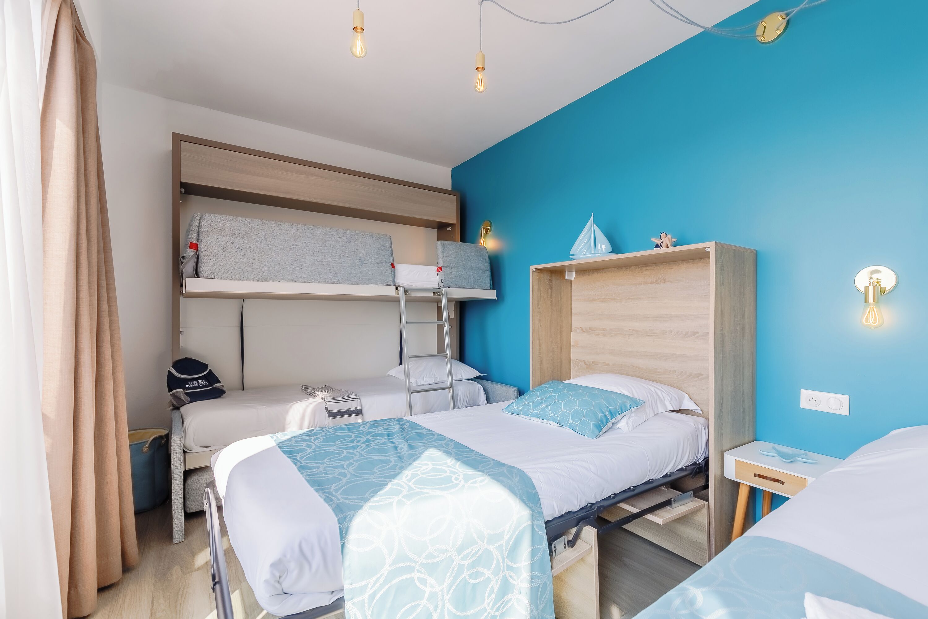 A compact hotel room with bunk beds, a desk, a chair, and a small bedside table.