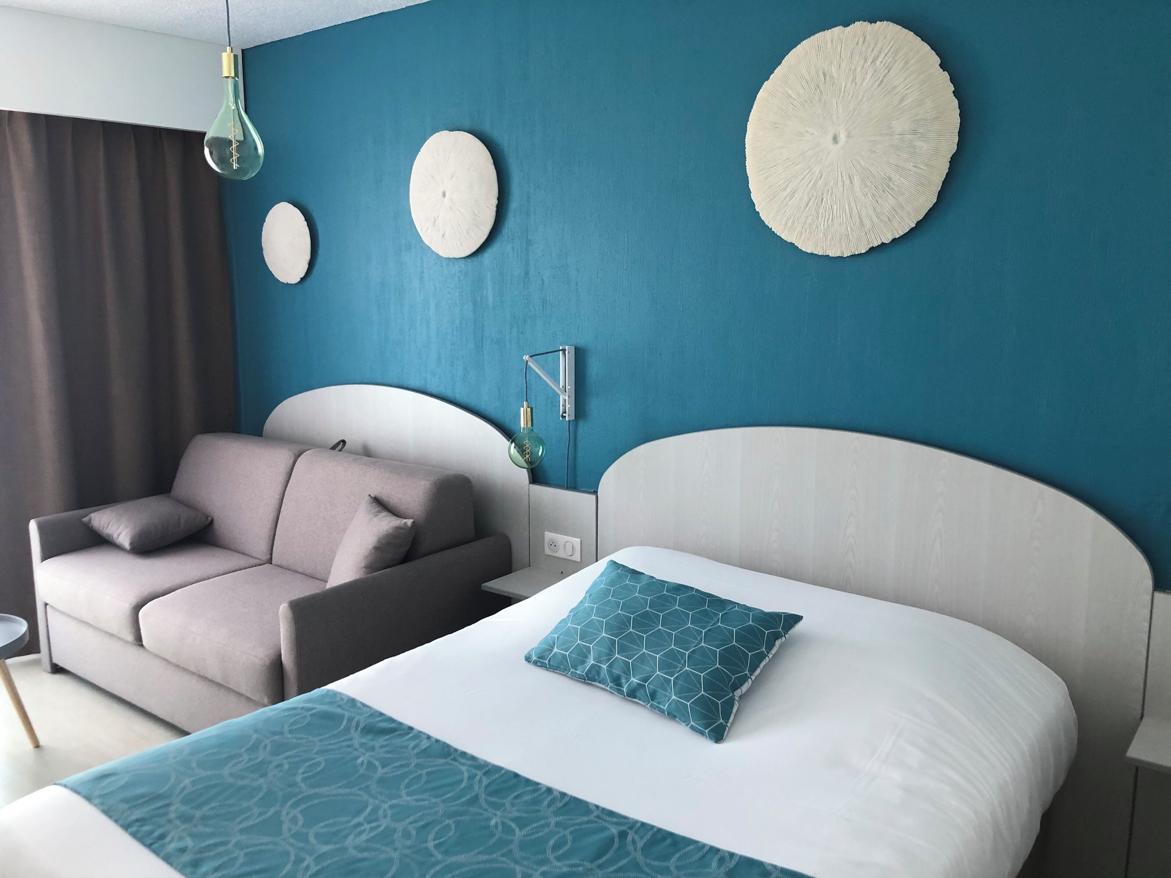 A modern hotel room with a bed, a sofa, and a wall with decorative items.