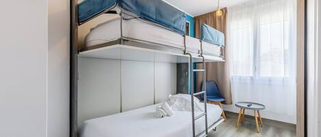 A bunk bed room with a small table and chair, a window with curtains, and a light fixture.